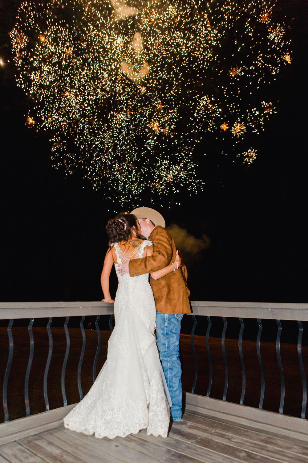 Golden fireworks illuminate the night sky as a couple embraces on a wooden balcony.