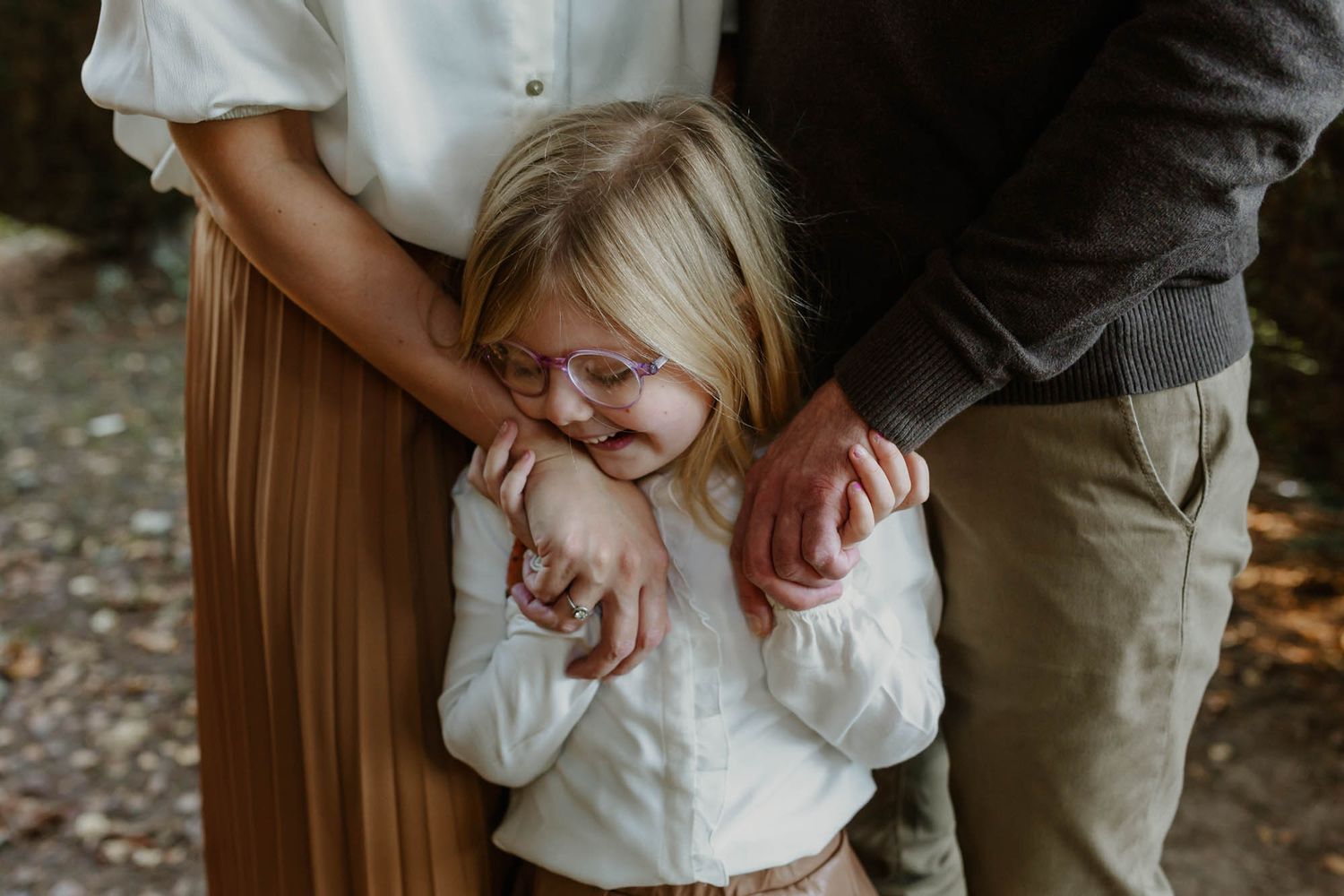 A candid family moment captured outdoors with parents holding their child in a warm embrace.