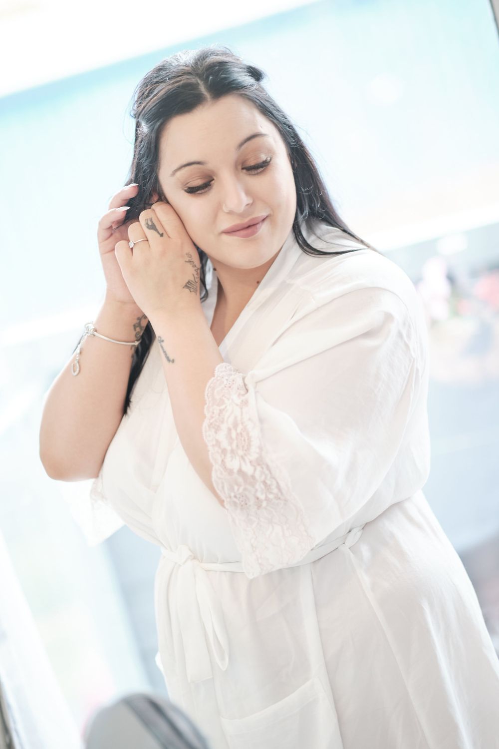 Person in white lace robe touches their hair while getting ready.