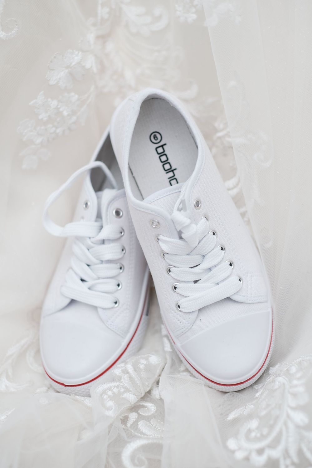 White canvas sneakers with red trim sitting on a lace-patterned surface.