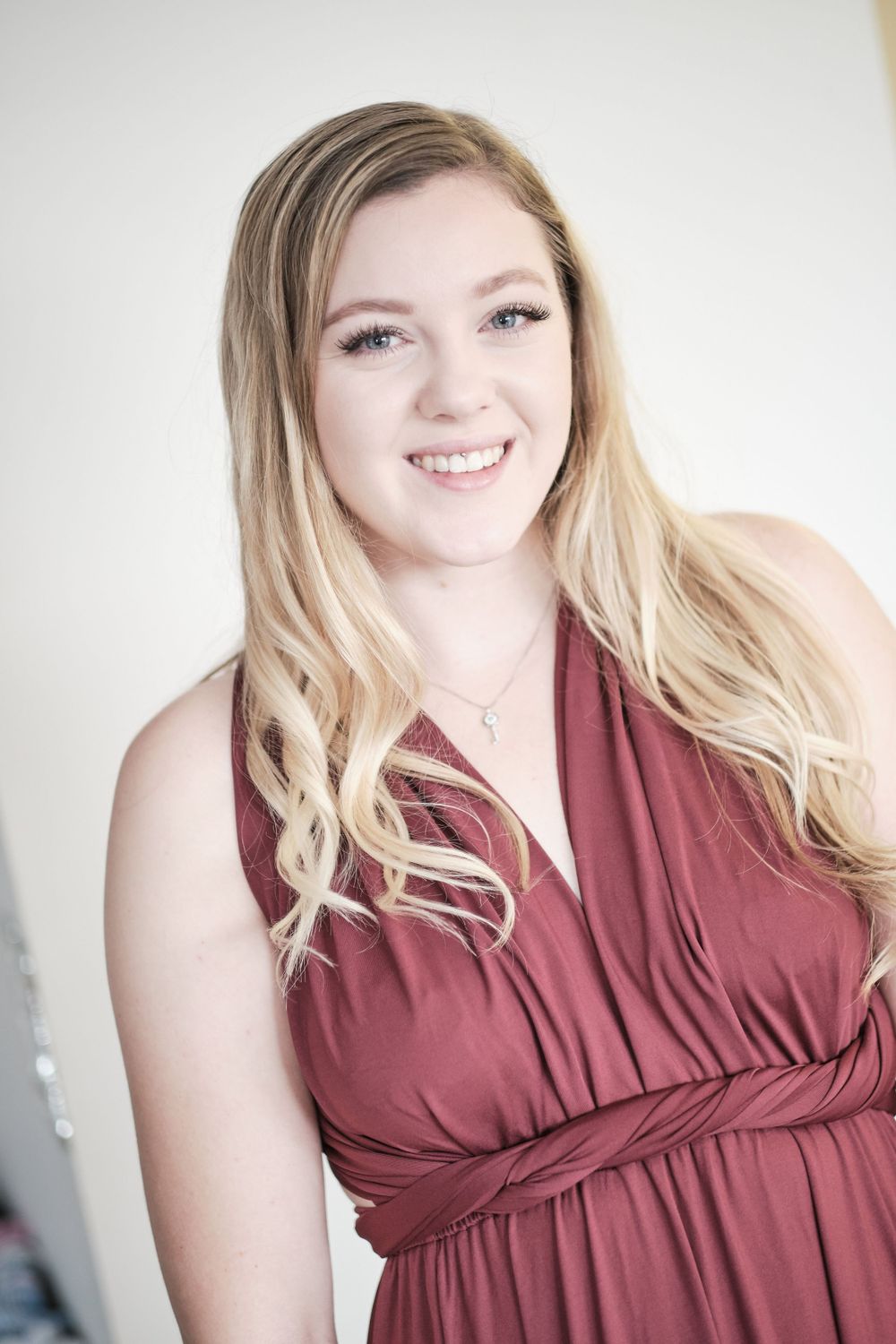 A person wearing a burgundy dress poses for a portrait with long wavy blonde hair.