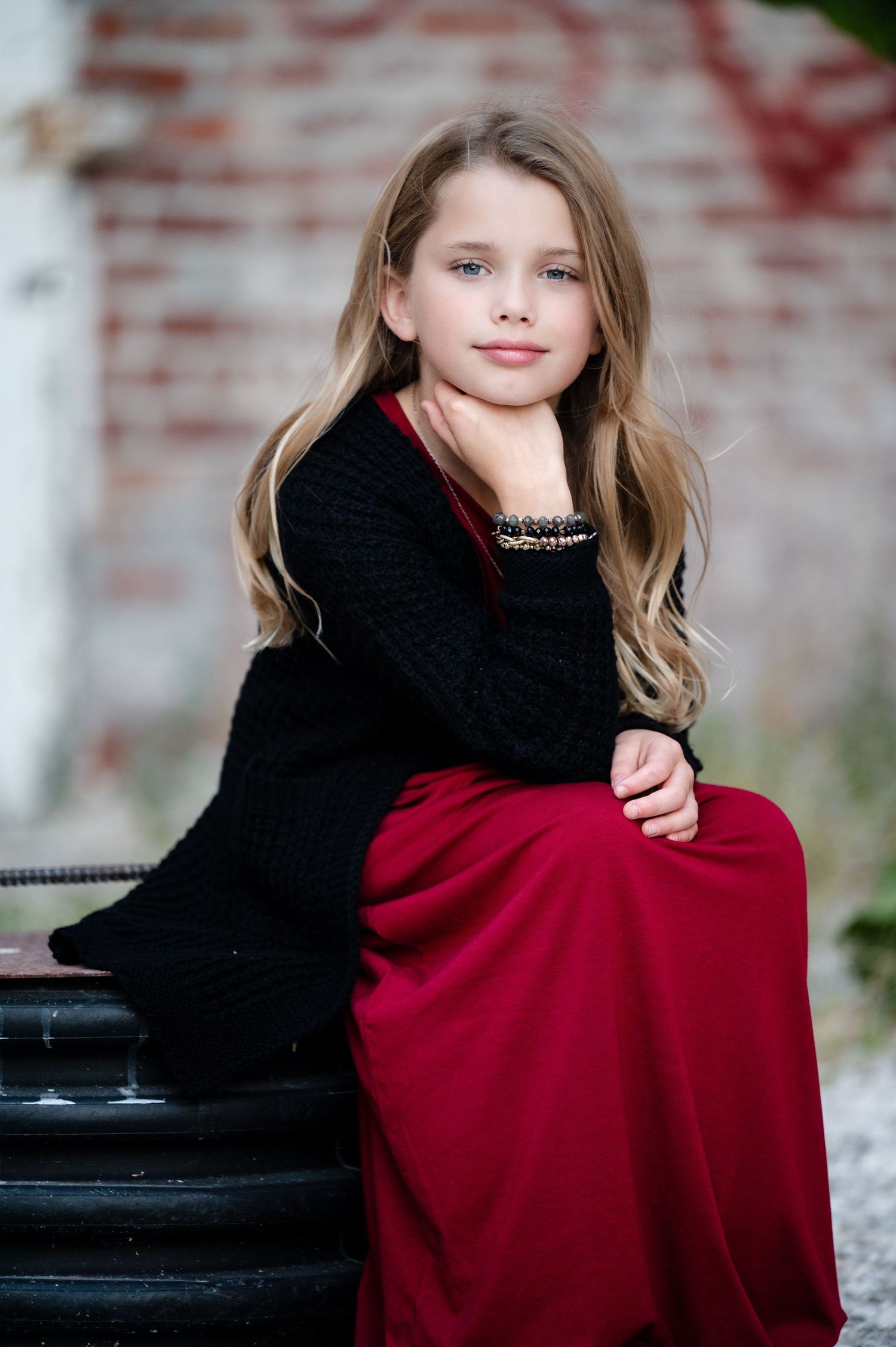 Portrait of a young person in a black sweater and red skirt sitting on a dark bench.