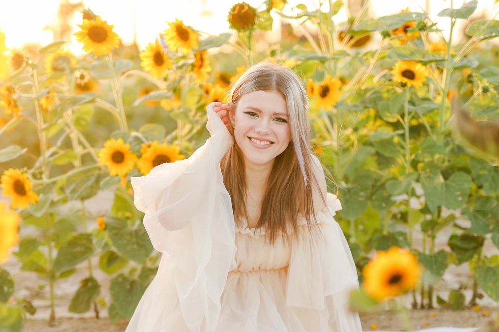 Young woman in cream sweater poses joyfully in front of sunflower field.