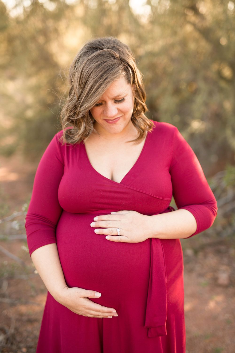 A woman in a red dress cradles her baby bump in warm desert lighting.