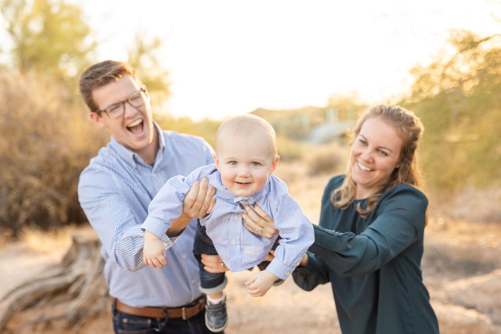 Parents playing with joyful baby outdoors in desert landscape.