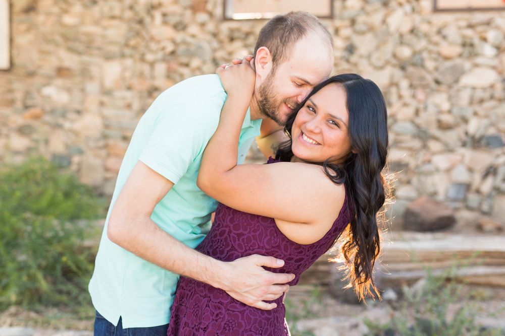 Romantic couple embracing and laughing against rustic stone wall.
