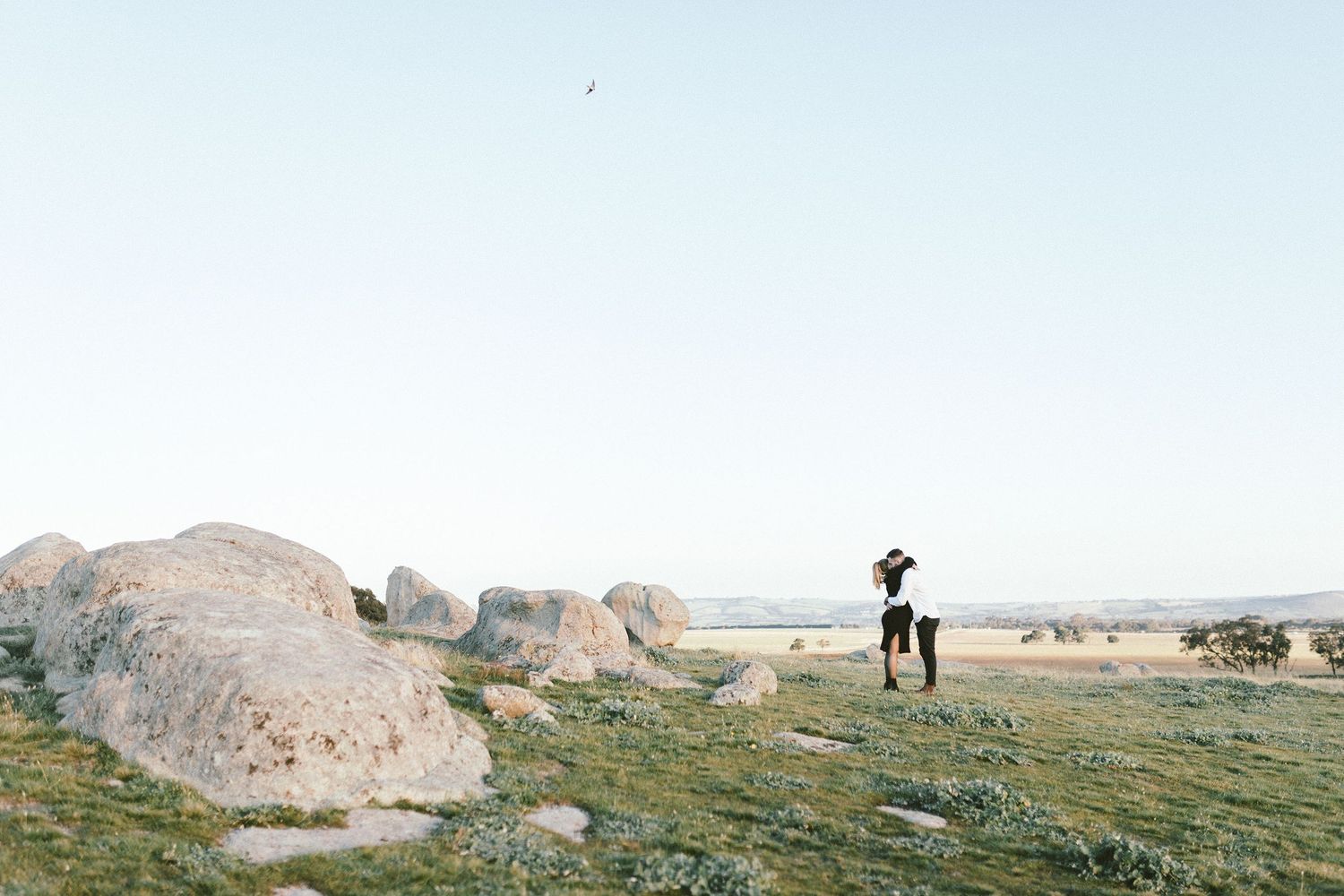A lone figure stands on a rocky outcrop overlooking a vast natural landscape at sunset.