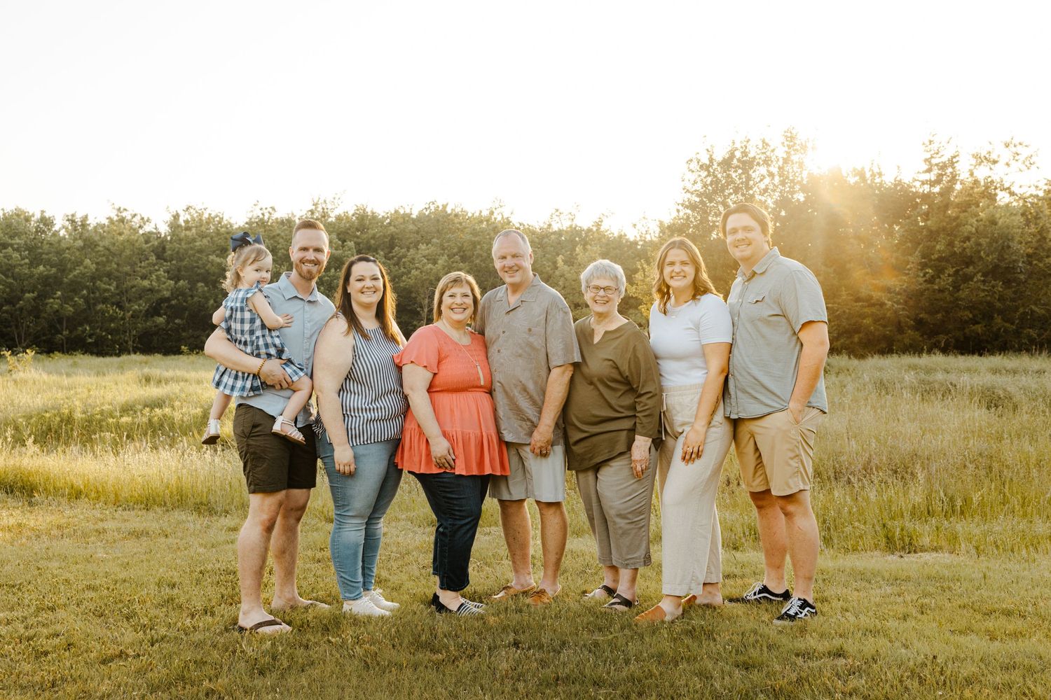 Family group poses together at sunset in a golden field during outdoor photo session.
