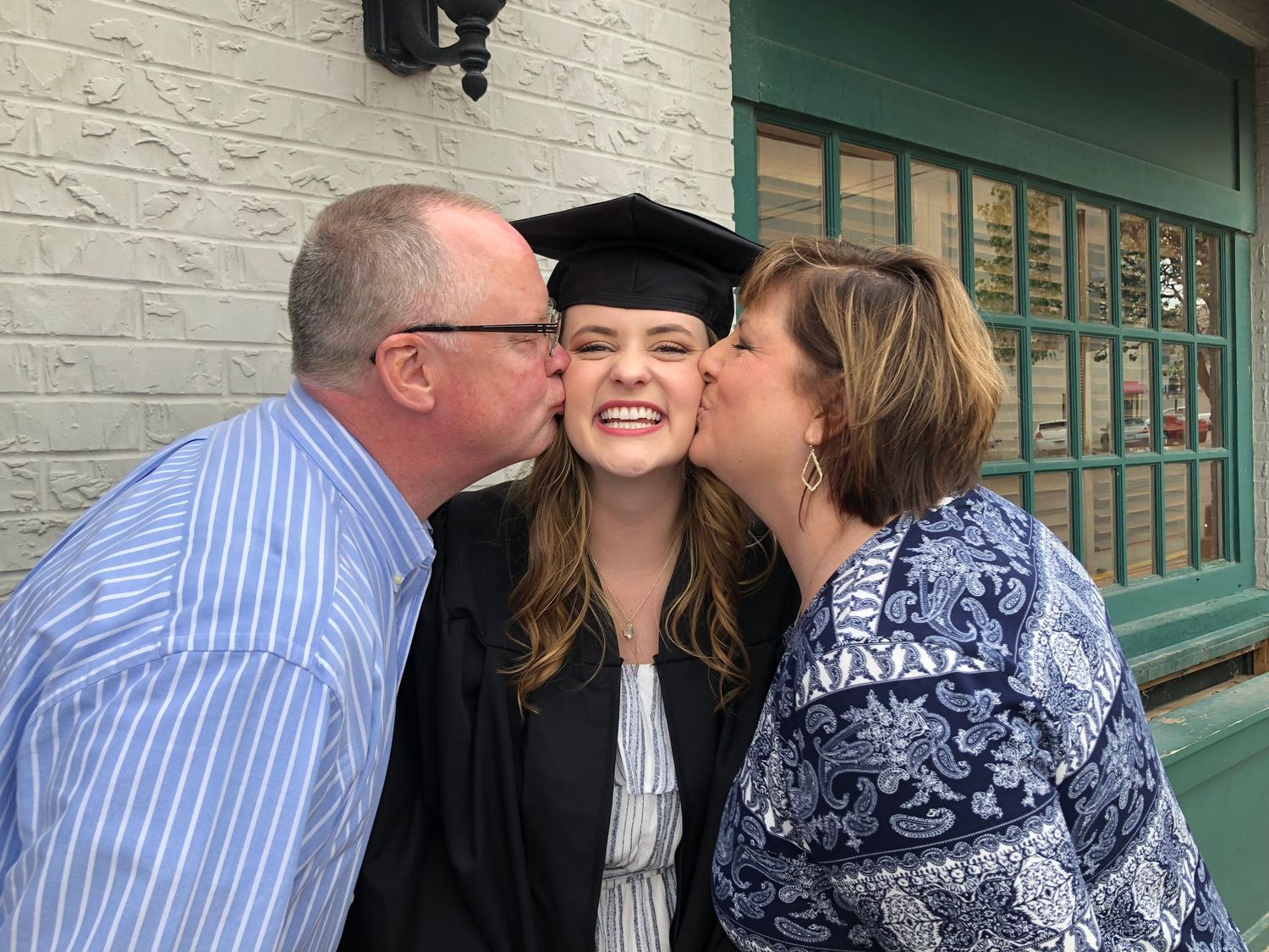 Graduate in cap and gown receives celebratory kisses during commencement ceremony.
