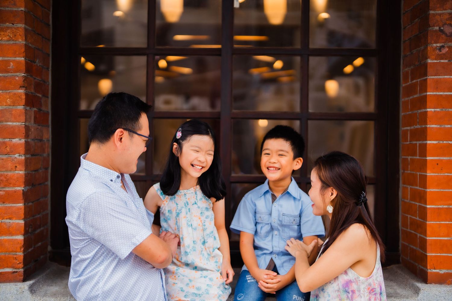 A family shares a candid laughing moment together in front of a glass door with warm lighting.