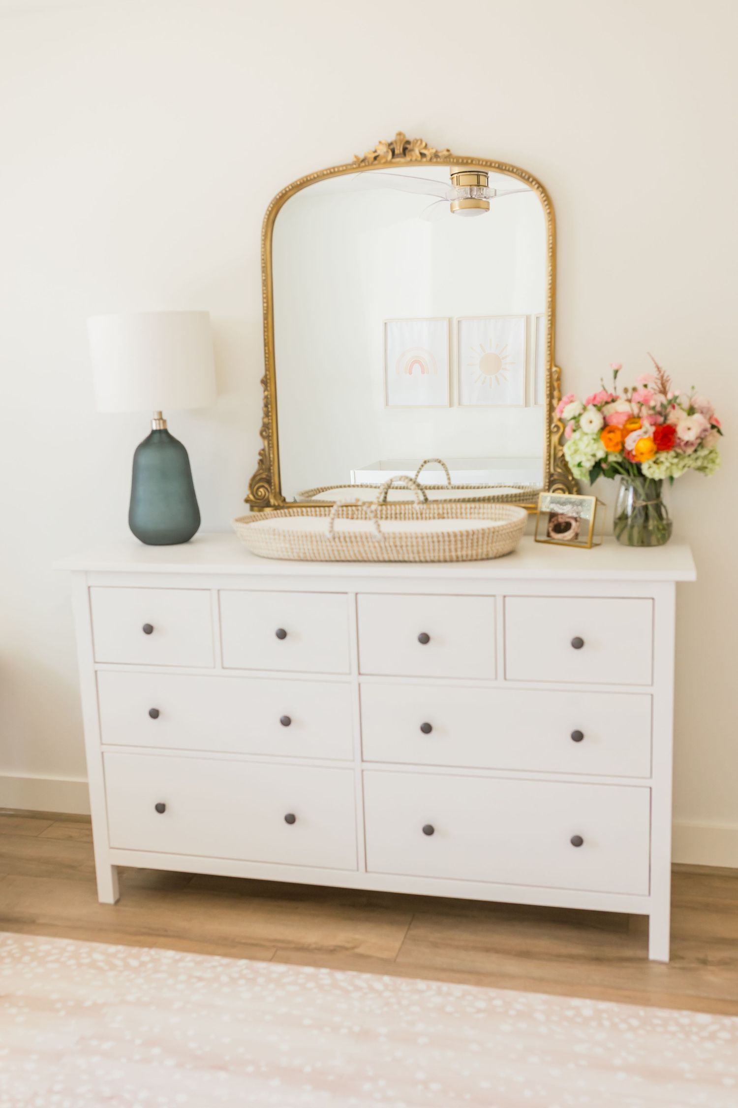 White dresser with gold mirror, teal vase and fresh flowers in nursery setting.