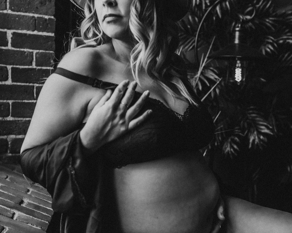 Black and white artistic maternity photo with dramatic lighting and foliage background.