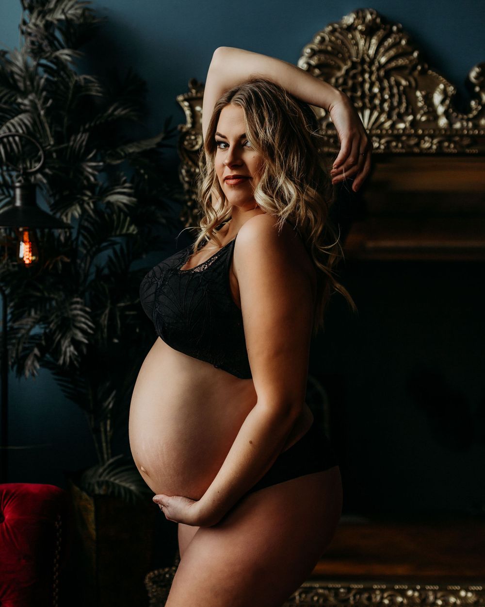 Side view maternity portrait against dark wall with decorative gold frame.