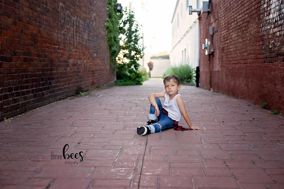 Child sitting in urban alley between red brick walls on stone pavement.