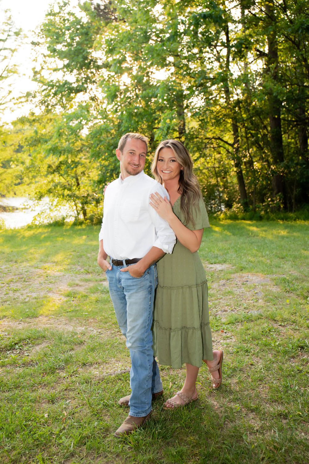 A couple poses together in a grassy field at sunset wearing coordinated casual outfits.