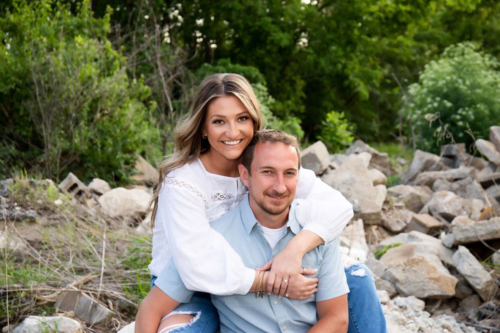 A couple poses together on rocky terrain surrounded by lush greenery in a casual outdoor photoshoot.