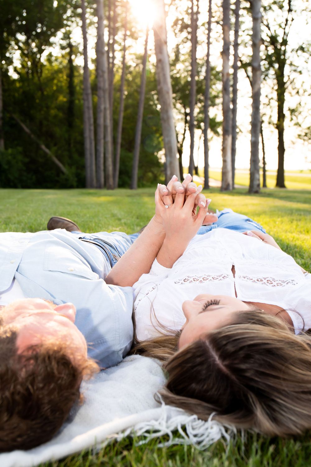 Couple lying in grass holding hands during golden hour sunset.