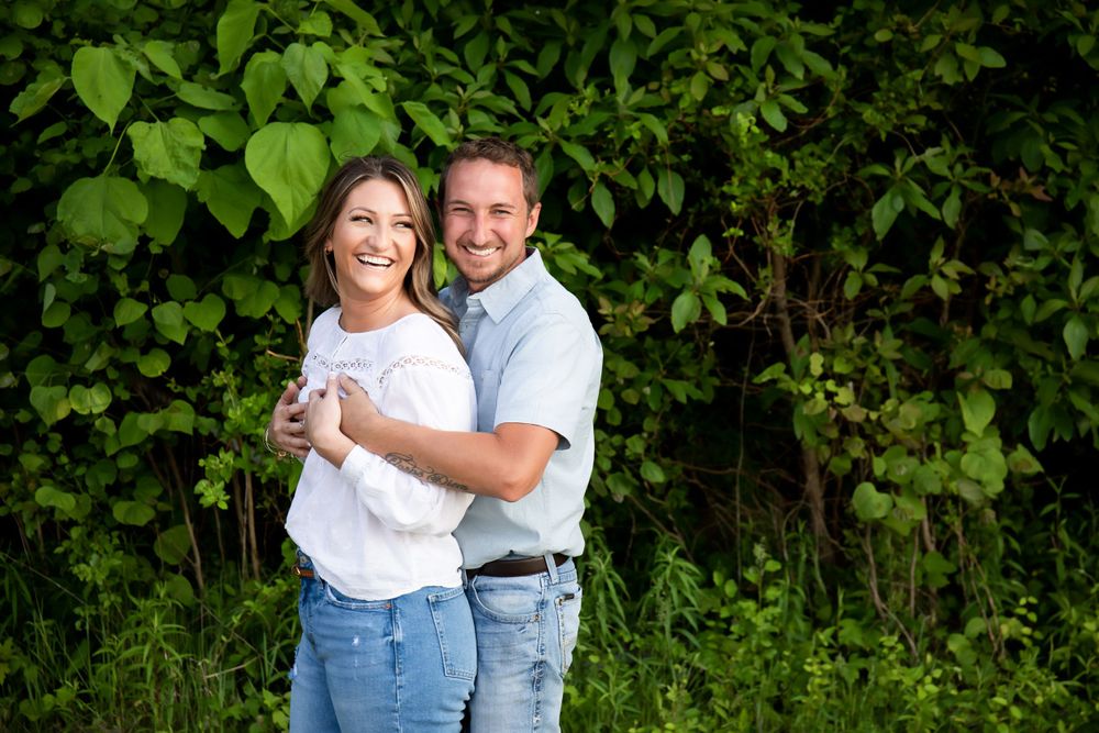 Happy couple embracing in casual outfits against lush green foliage.