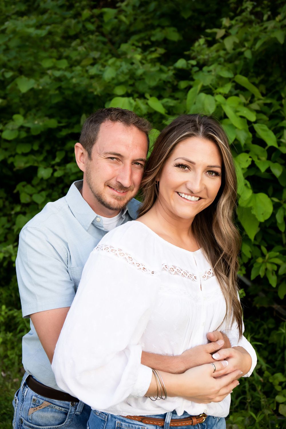 Romantic outdoor portrait of couple in white and blue against green leaves.