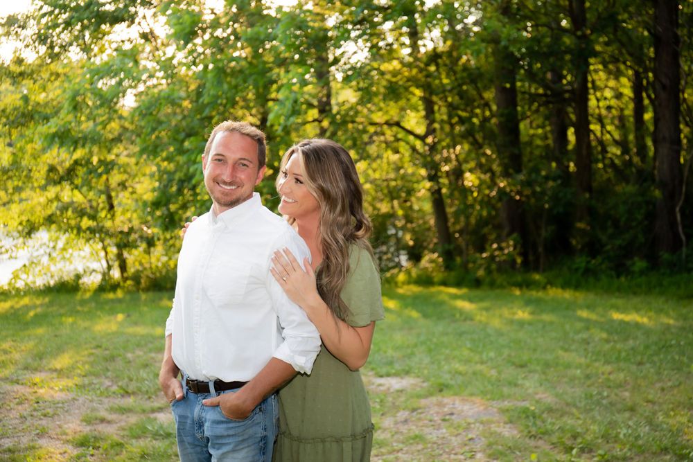 A couple poses together in a sunlit field during golden hour for their engagement photos.