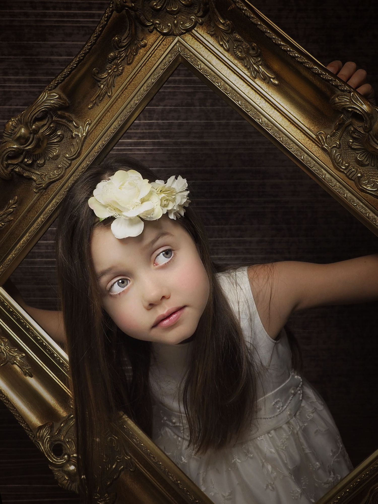 portrait of a gile with brown hair looking through a gold frame