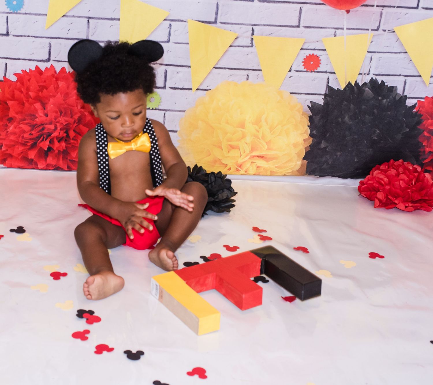 Party setup with red and yellow pom poms against a brick wall backdrop.