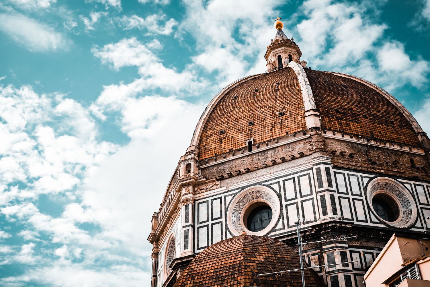 Dramatic view of the Florence Cathedral dome against turquoise sky with white clouds.