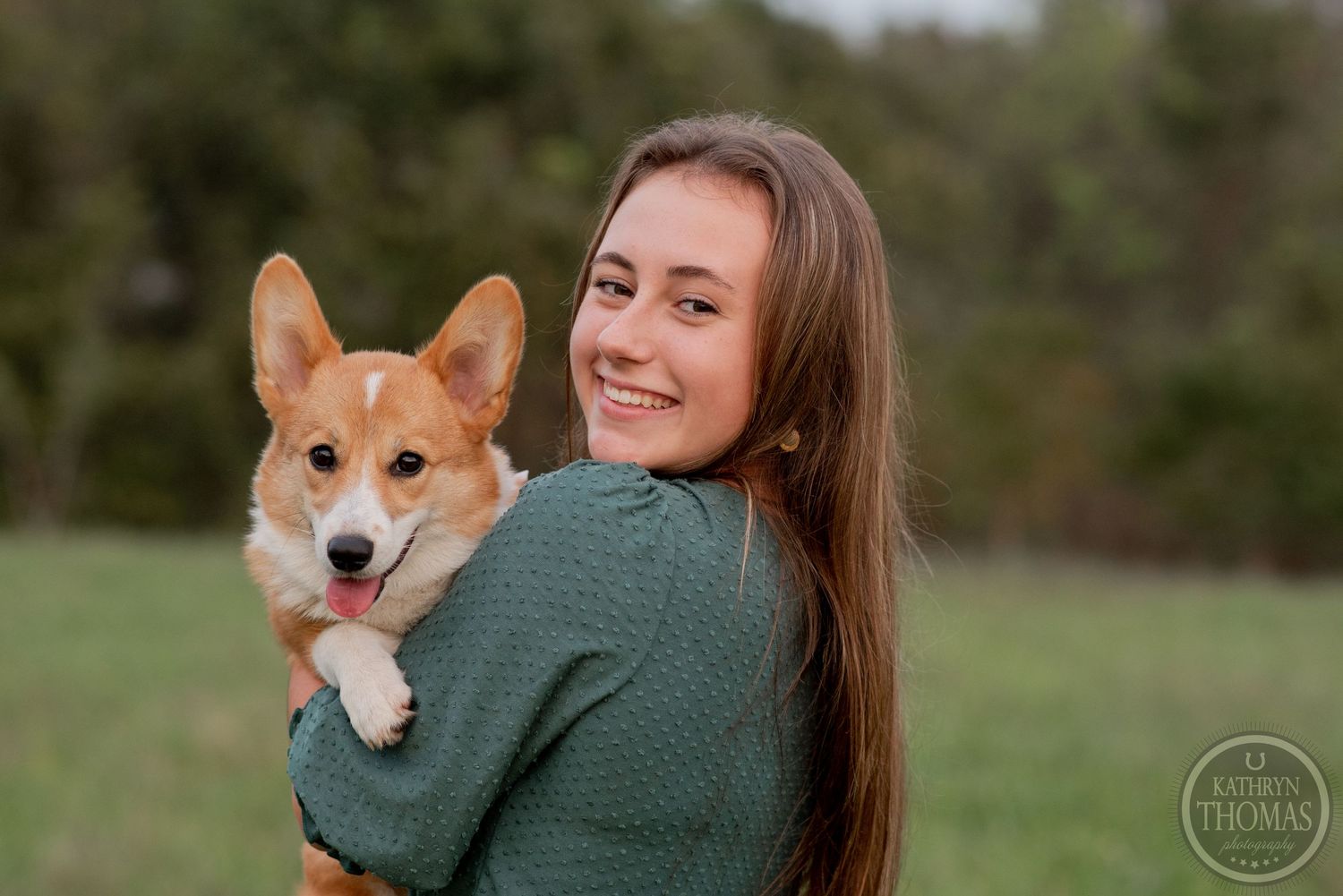 Happy Corgi puppy being held while posing for an outdoor portrait.