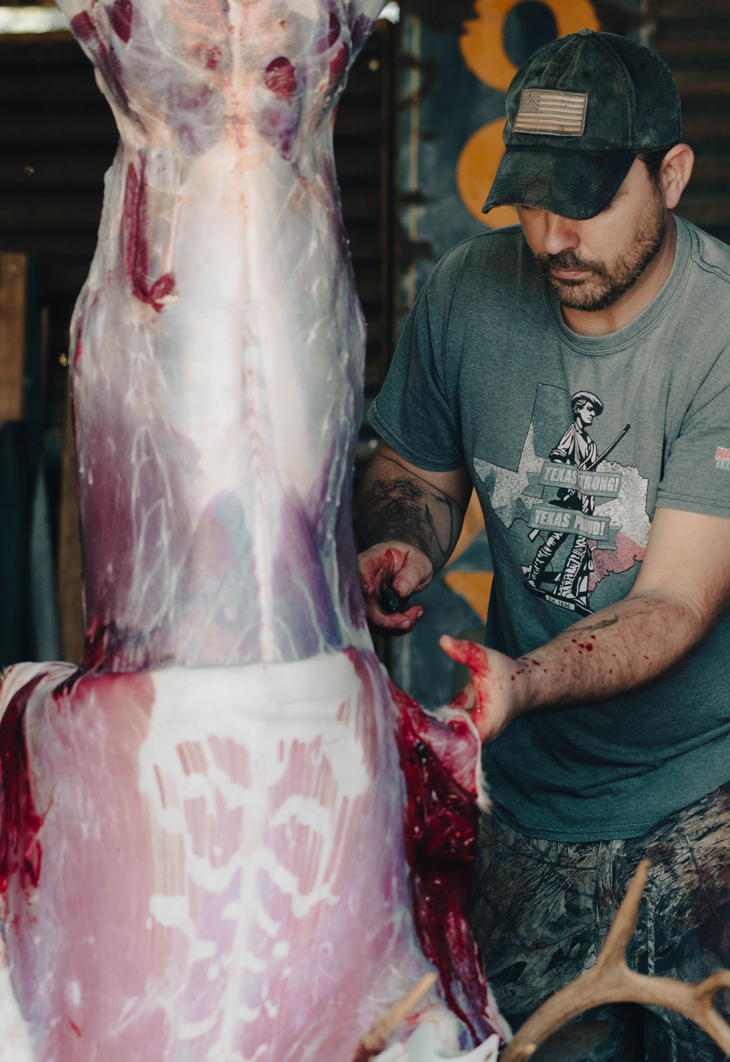 Butcher in gray t-shirt carefully processes a large animal carcass in a food preparation area.