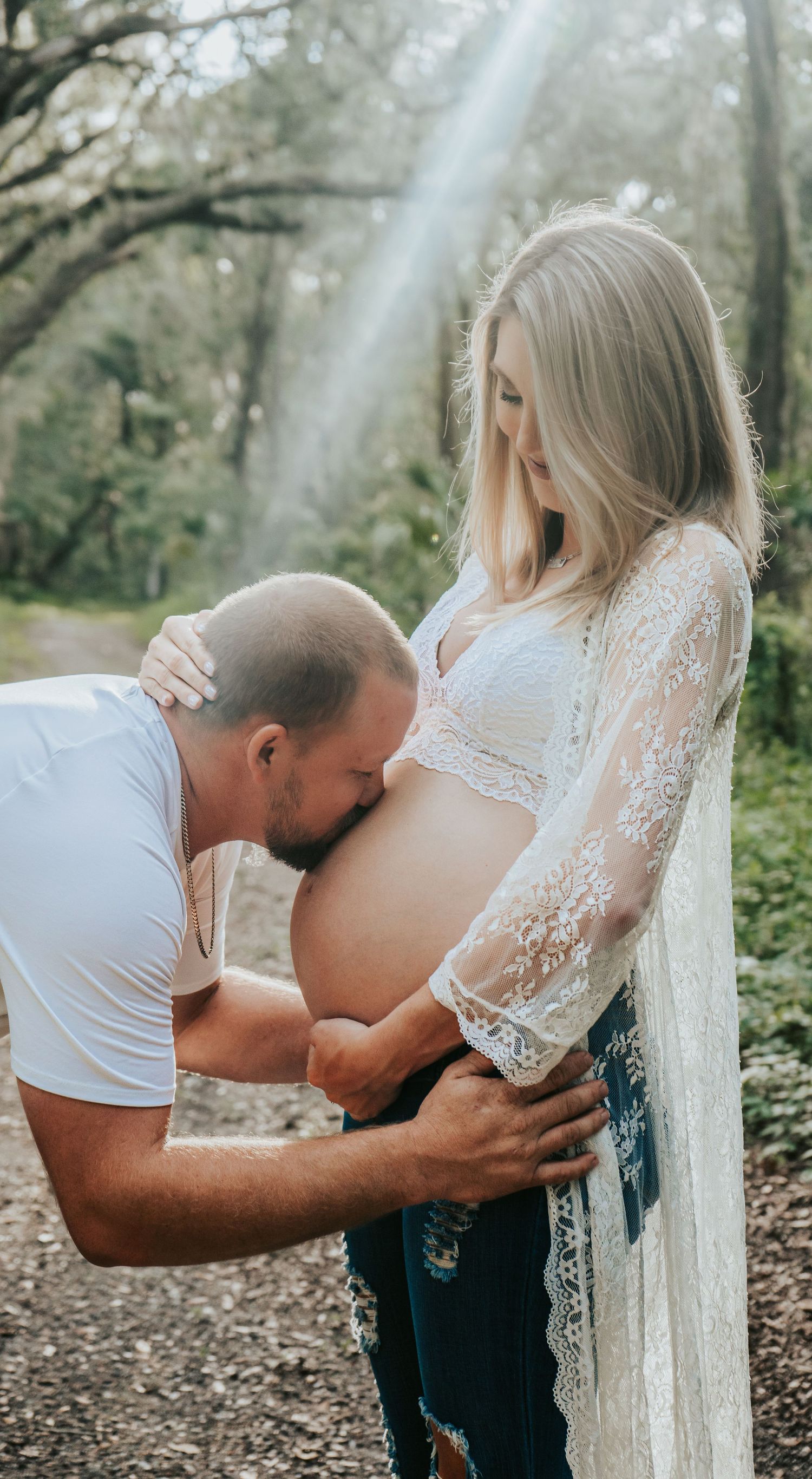 Outdoor Maternity Session at Thatcher Park, Lithia, FL; husband kissing pregnant wife's belly bathed in sunlight