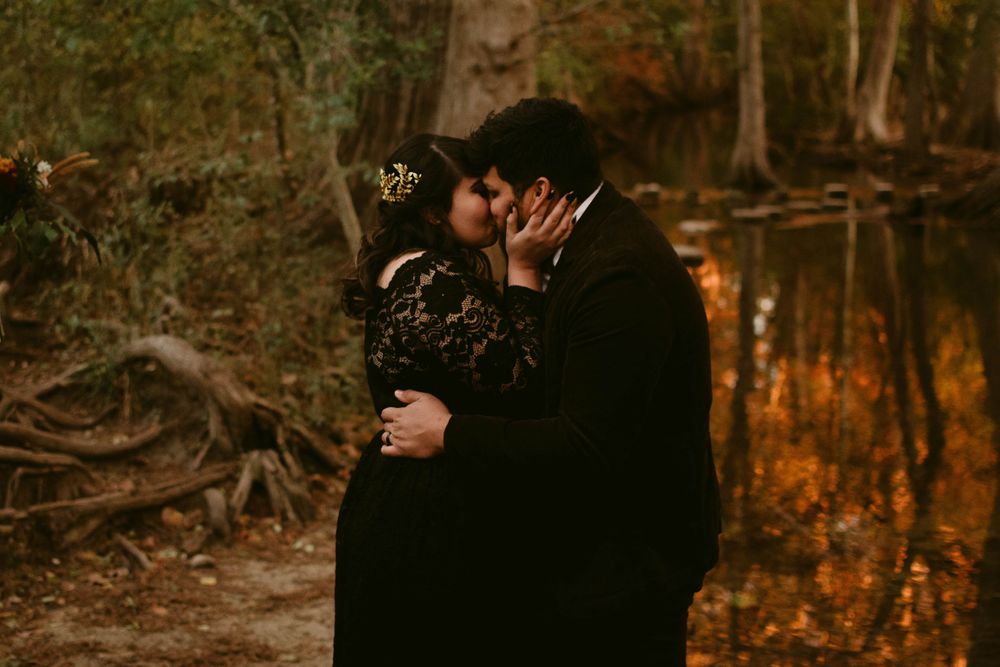 Romantic embrace between couple in black attire during forest wedding.