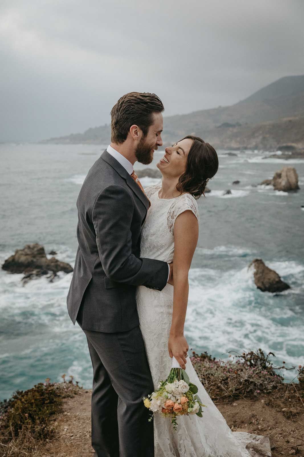 Romantic wedding portrait on a cliff edge with crashing waves and coastal scenery.