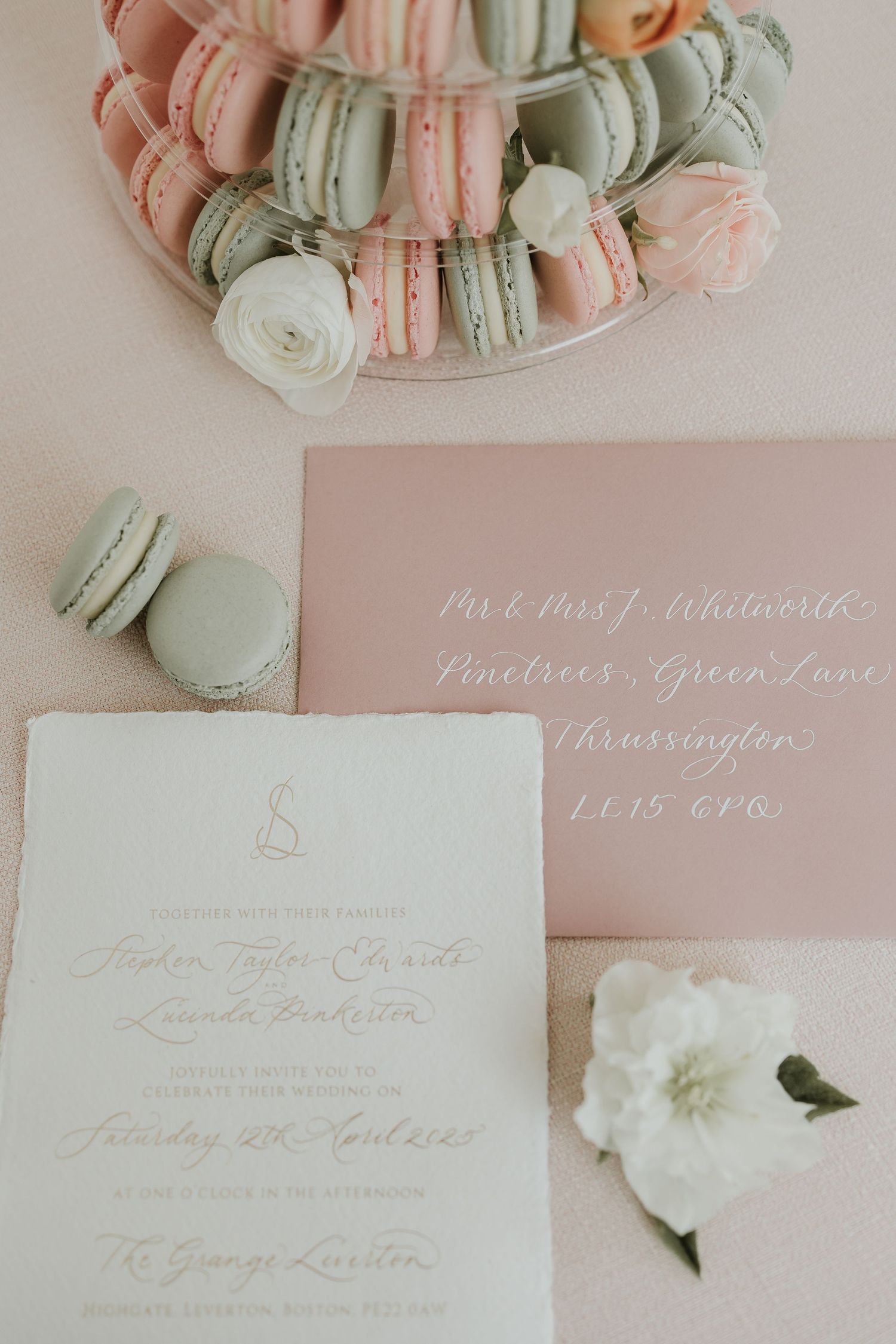 Wedding invitation suite with pink and mint macarons and white floral accents.