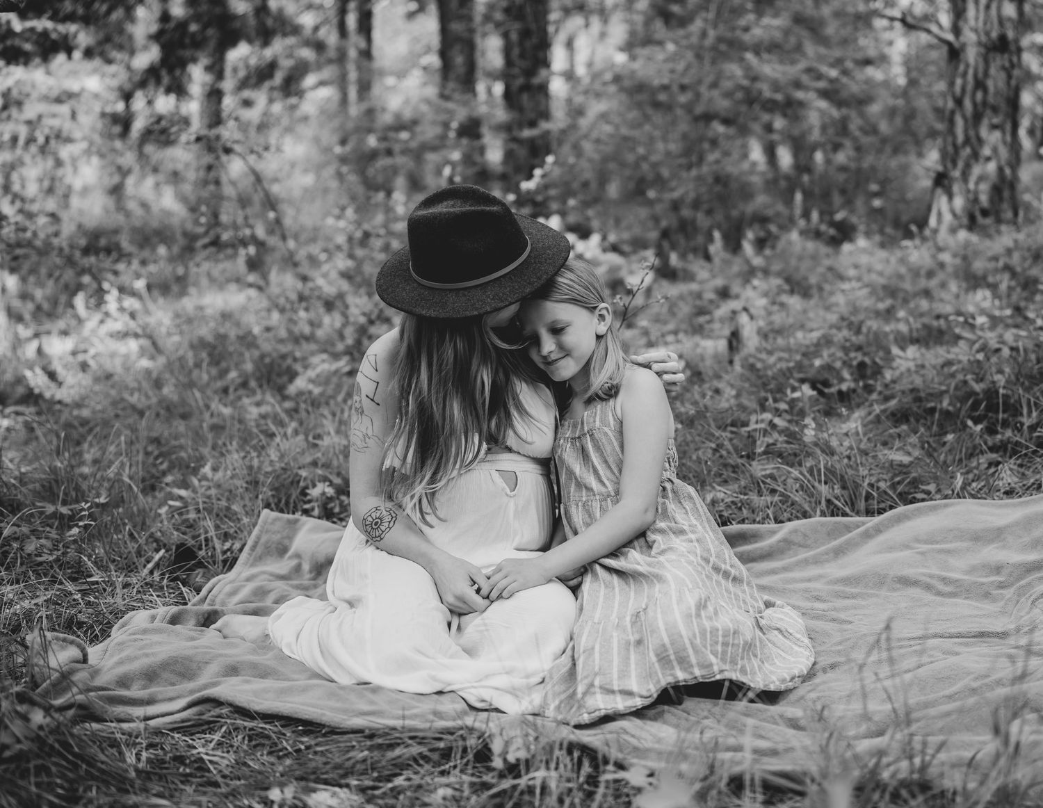 Black and white photo of two people sitting together on blanket in forest setting.