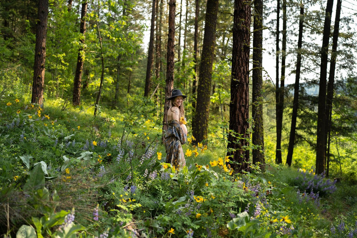 Person standing among yellow wildflowers in sunlit forest clearing.