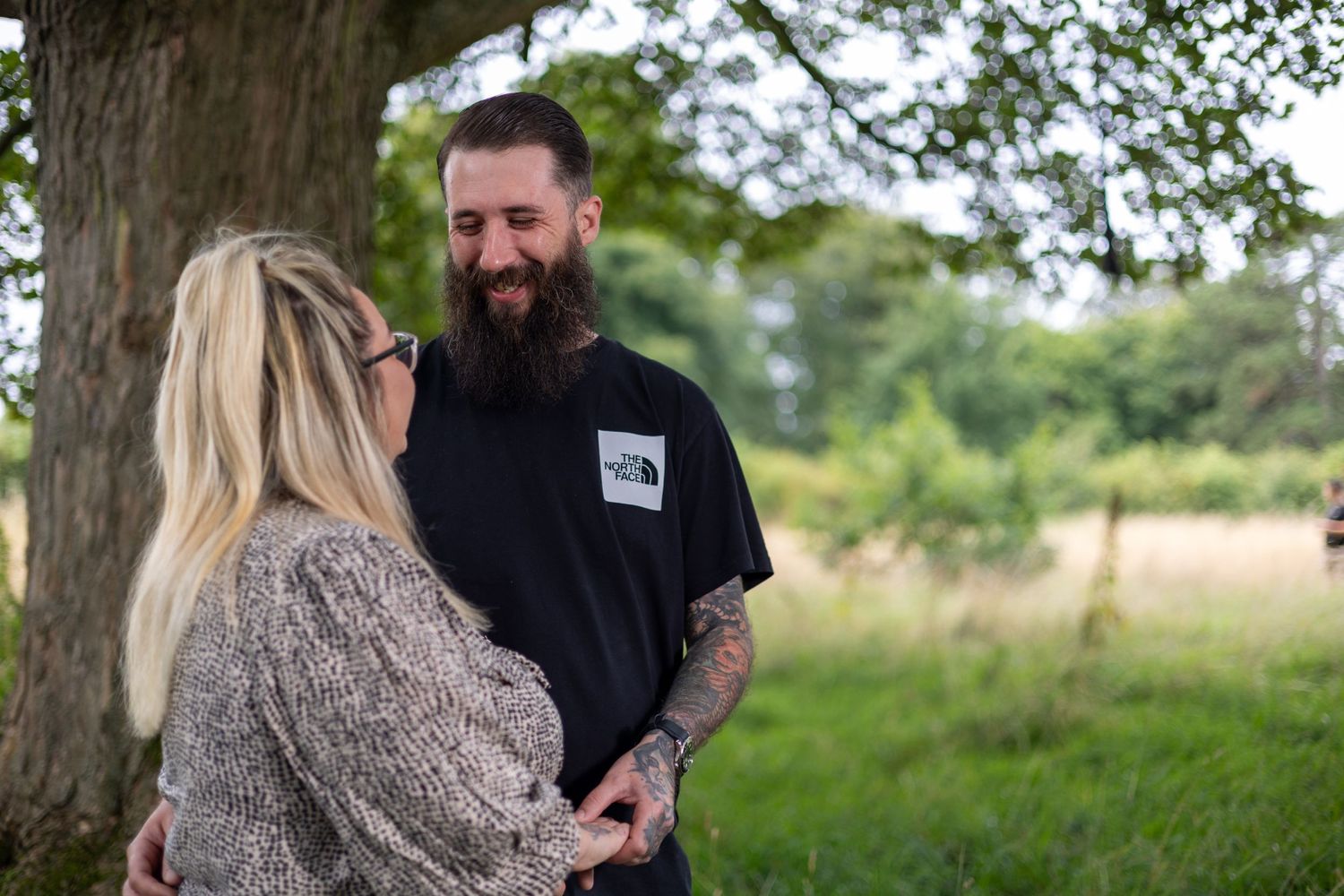 A couple shares an intimate moment in a lush outdoor setting with green foliage in the background.