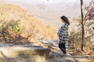 Silhouette of pregnant woman standing on rocky outcrop with autumn mountain vista.