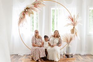 Family portrait session with gold arch and pampas grass decorations in bright white room.
