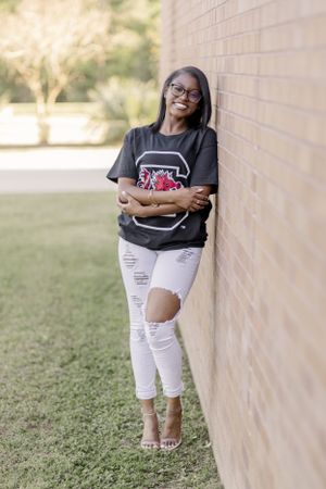 Student in ripped jeans and graphic tee poses against brick wall on campus.