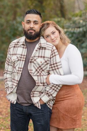 Couple in autumn attire posing together against natural foliage background.