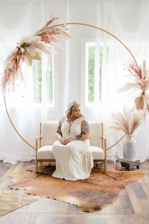 Bridal portrait with circular gold arch and pampas grass decorations in bright white room.