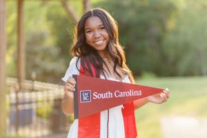 A student displays a University of South Carolina pennant while standing outdoors in natural lighting.