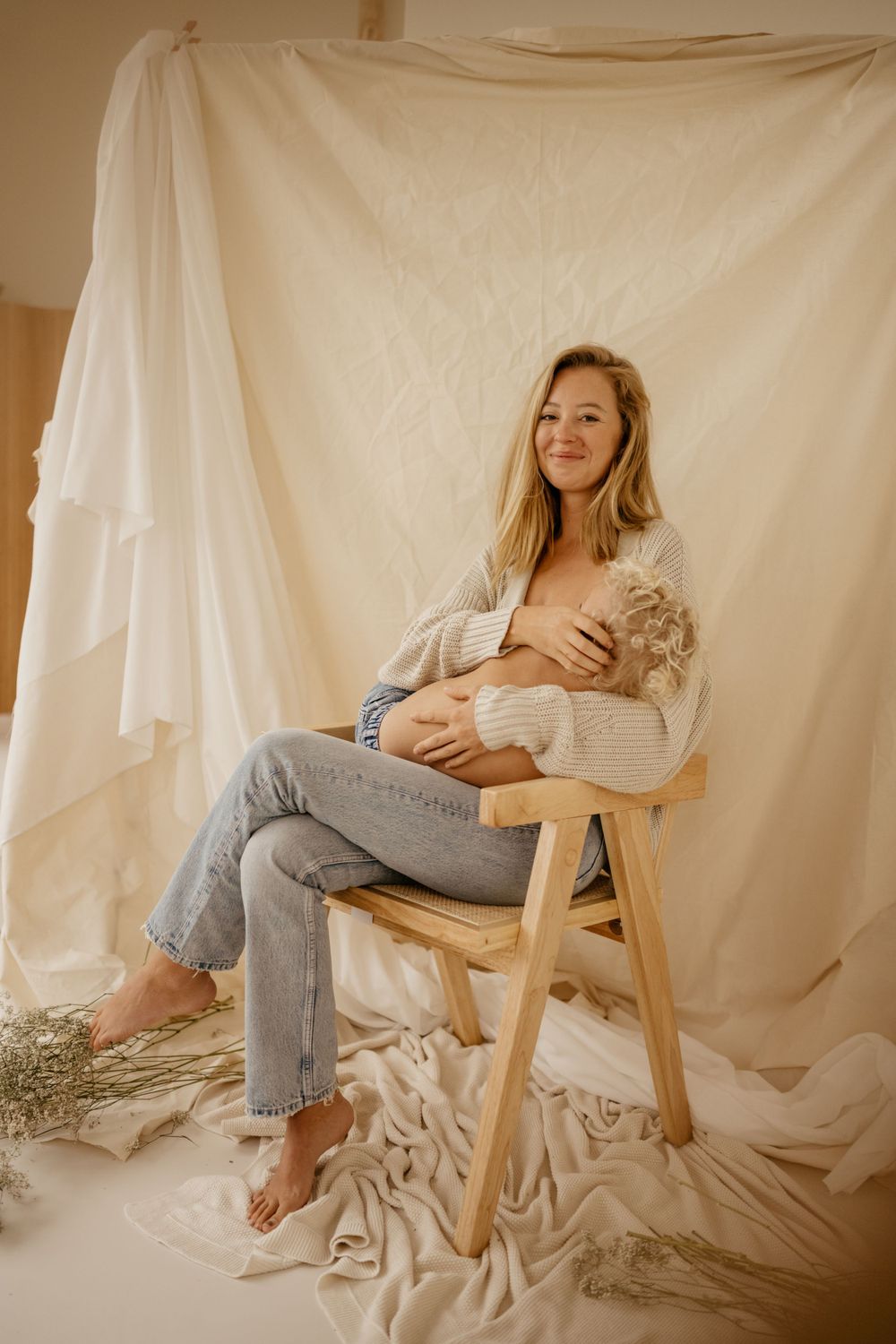 Woman in casual attire sits on wooden stool against white backdrop for intimate portrait session.