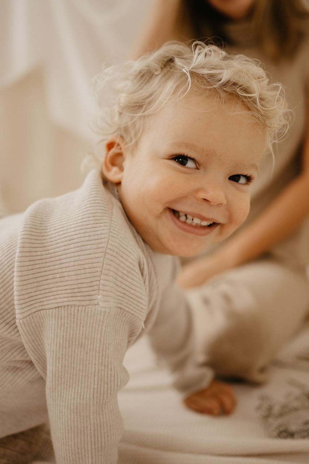 Close up of toddler in cream sweater with bright smile.