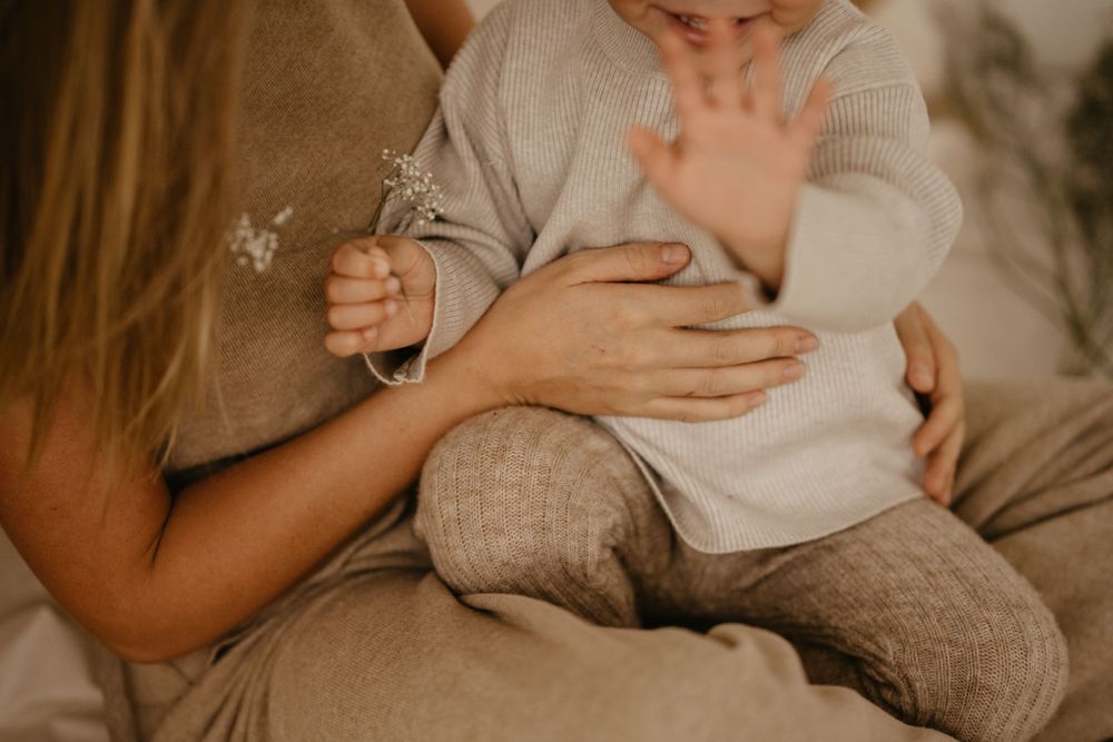 Gentle hands tenderly hold a small infant wrapped in soft knit clothing.
