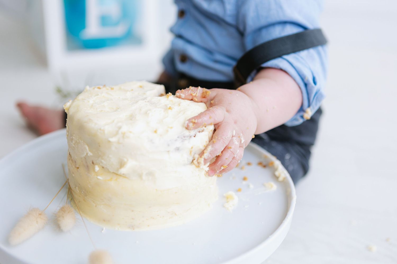 Small hands reaching to touch a frosted white cake on a plate.