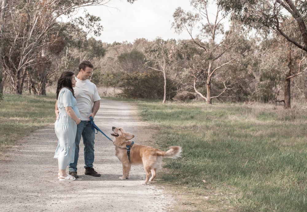 A couple and their dog share a tender moment in a rustic outdoor setting during golden hour.