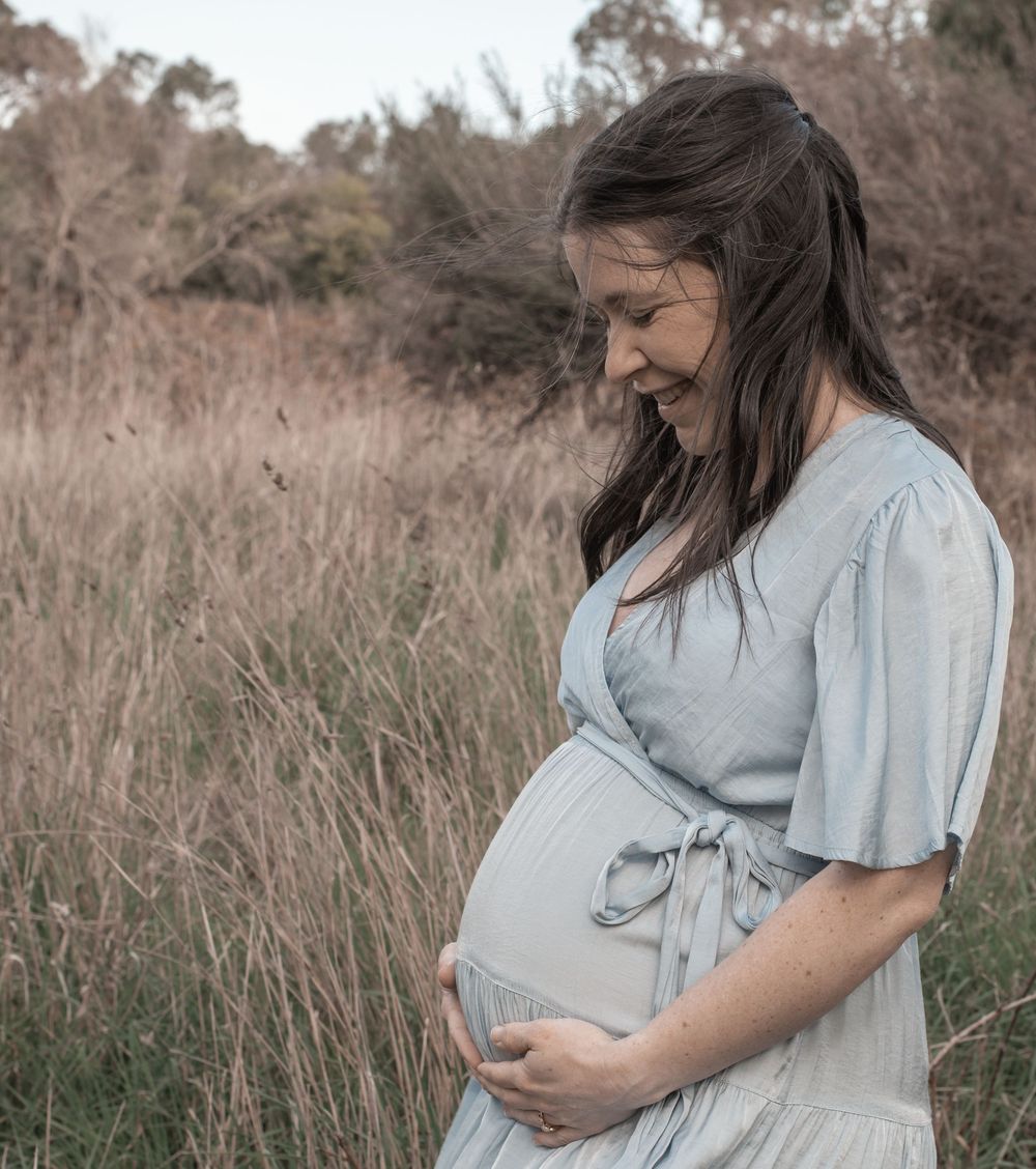 A series of maternity photos showing a woman in a light dress cradling her baby bump in a rustic outdoor field setting.