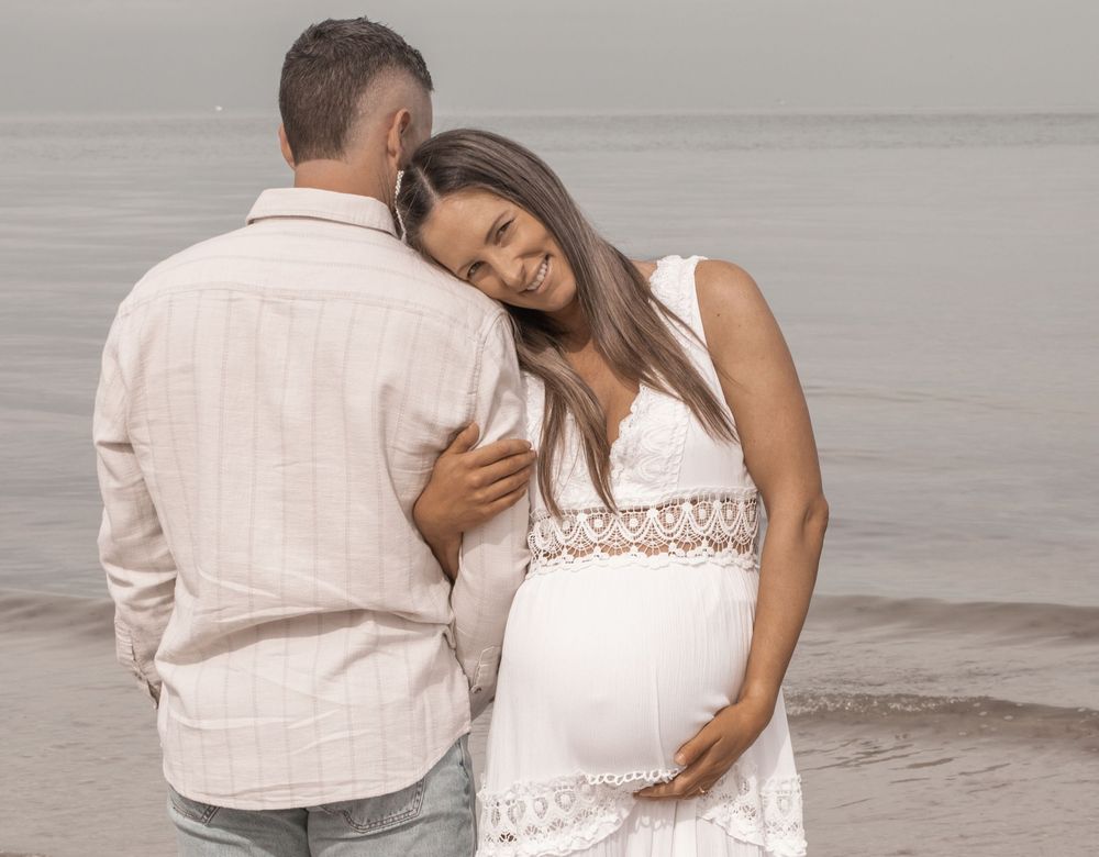 Romantic couple embraces on a misty beach while wearing white and beige casual attire.