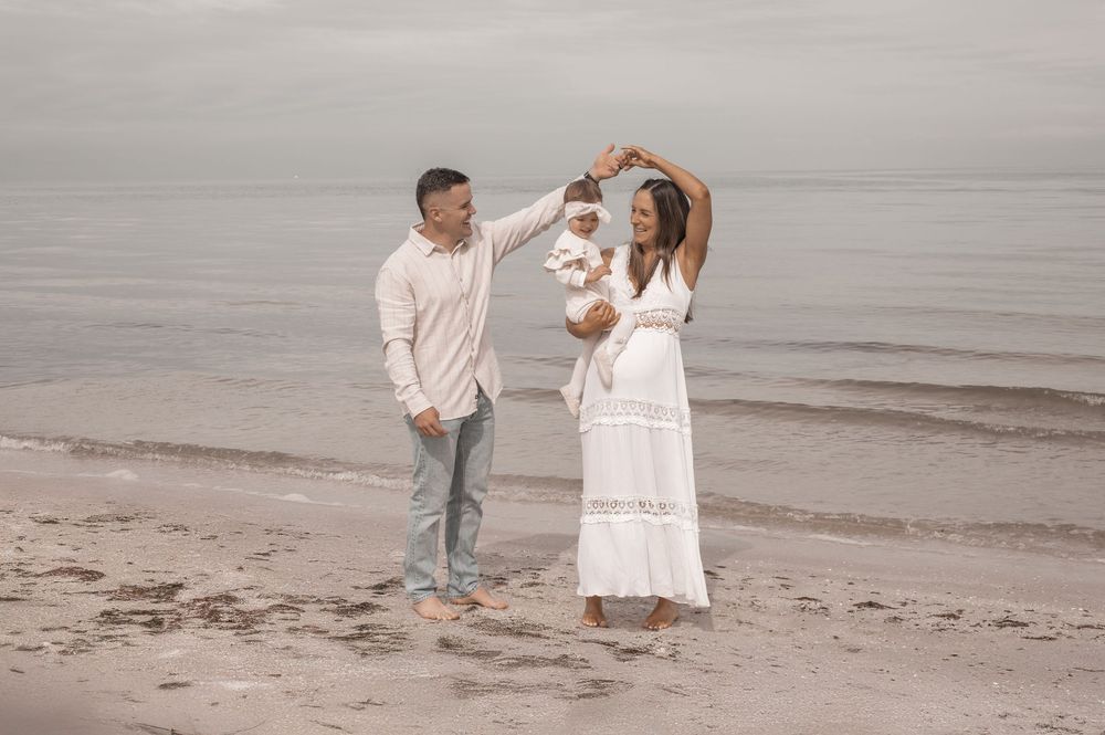 Family walking together along the shoreline wearing white outfits on an overcast beach day.